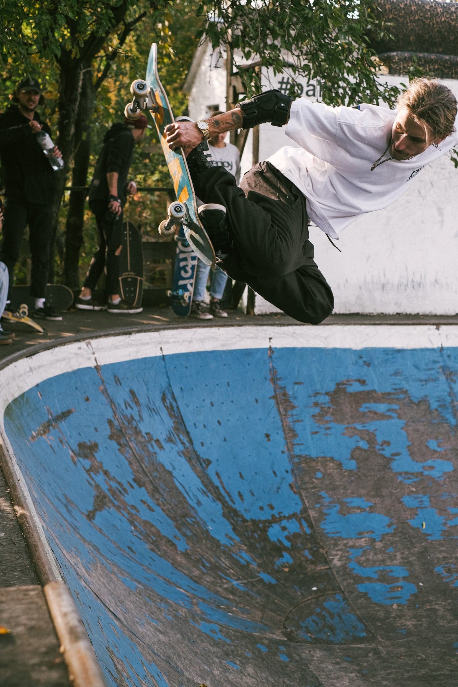 Skateboarder grabbing his board above the coping of a weathered blue bowl