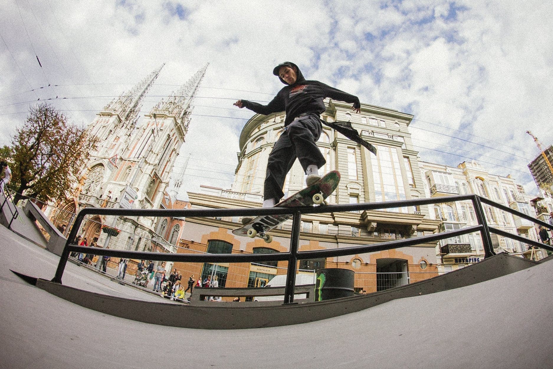 Skateboarder sliding a rail on a city plaza with a gothic cathedral behind him