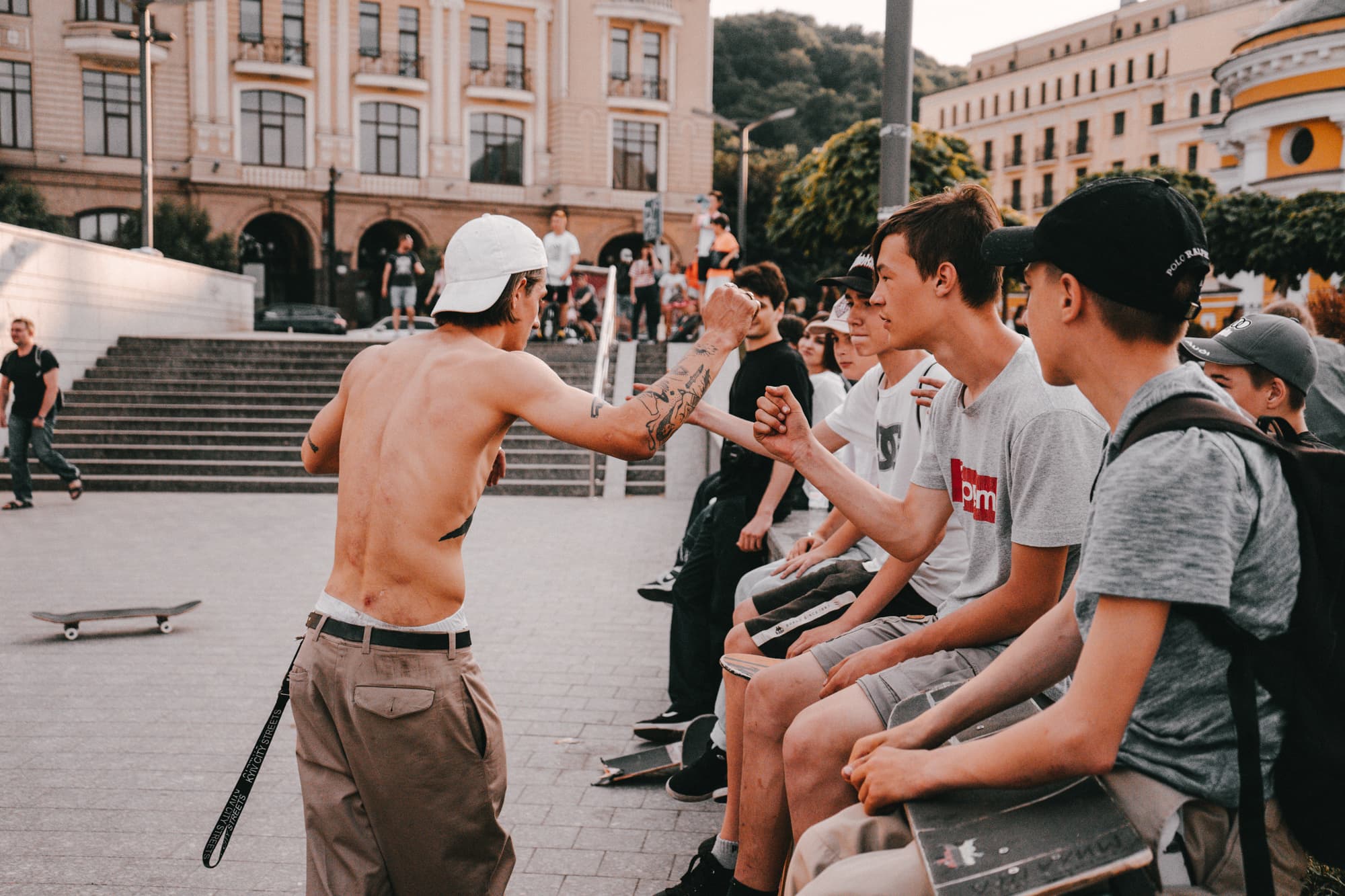 Fist bumps down a line of young skaters sitting on a ledge at a city plaza session