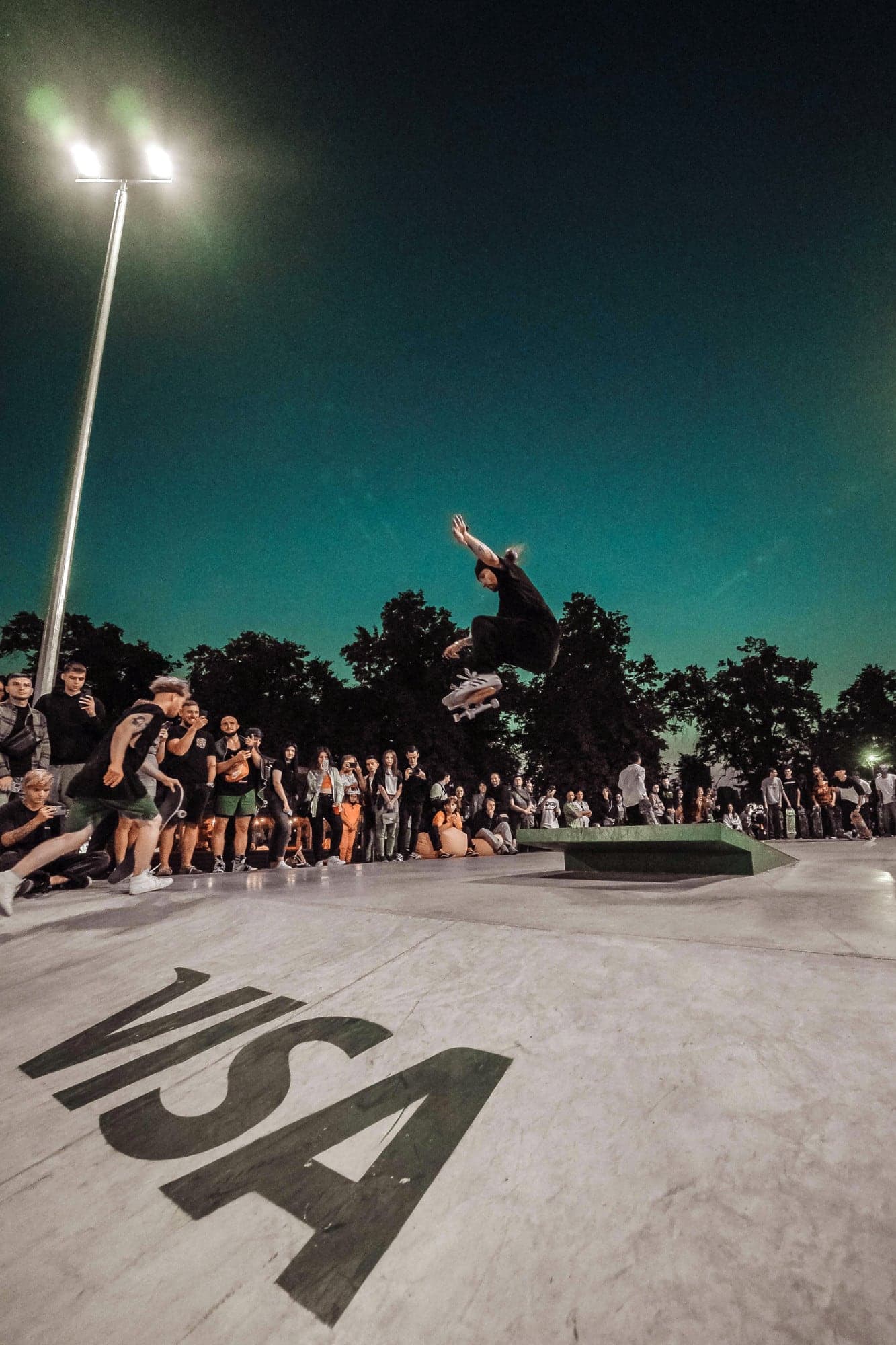 Skateboarder mid-air over a ledge at a floodlit night contest