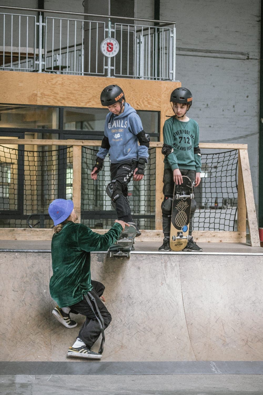 Coach crouched at the base of a ramp guiding two helmeted students as they drop in