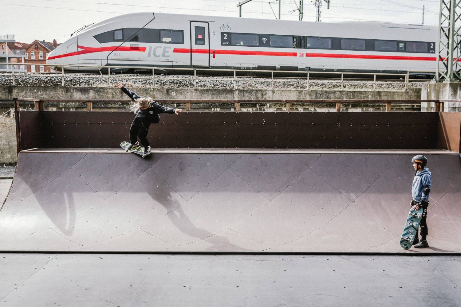 Skater carving the quarterpipe as an ICE train passes the park behind in Hannover