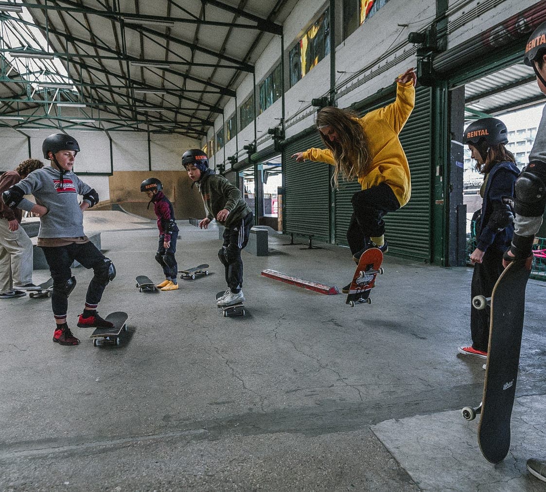 Kids practising the basics on the flat while a coach ollies past at the covered skatepark